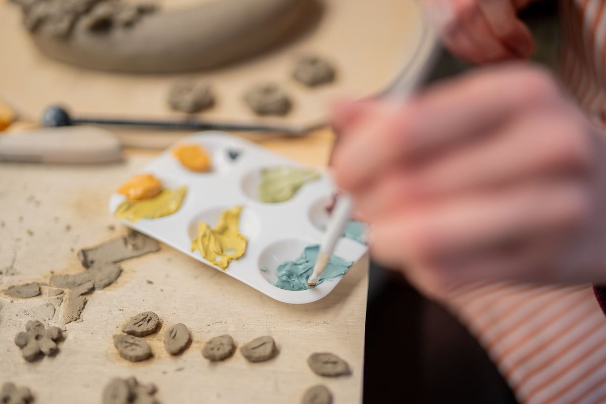 Person painting small ceramic pieces on a table with a palette of colors.