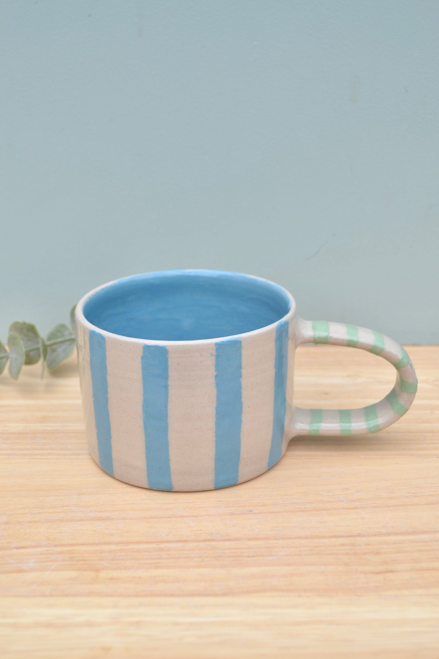 Mug with blue and beige stripes on a wooden surface with a light gray background