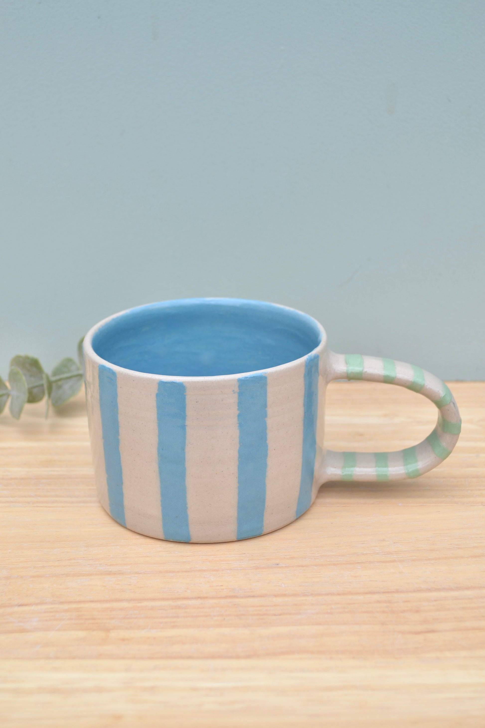 Mug with blue and beige stripes on a wooden surface with a light gray background