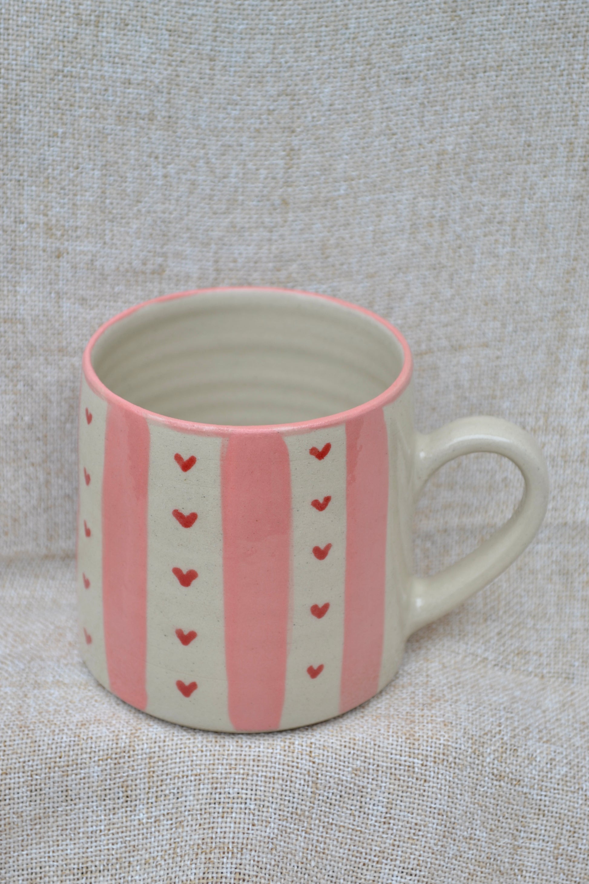 Ceramic mug with pink heart patterns on a textured gray background