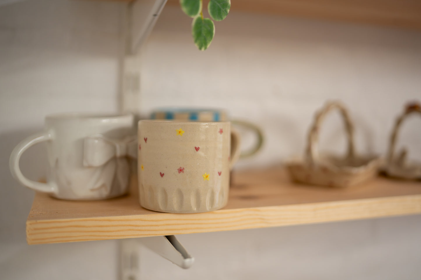 Two ceramic mugs on a wooden shelf with a blurred background