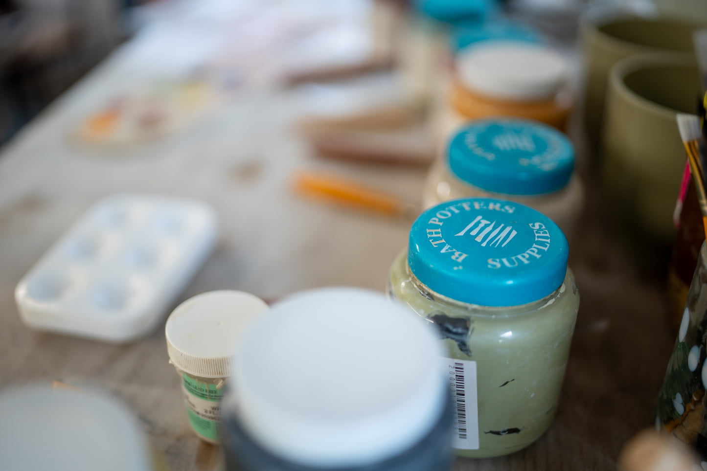 Jars of paint with blue lids on a table, likely in an art studio setting.