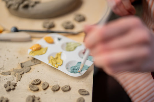 Person painting small ceramic pieces on a table with a palette of colors.
